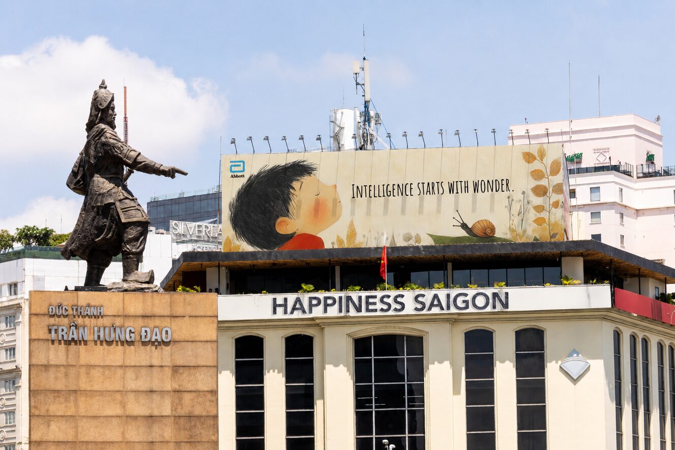 A large outdoor campaign panel reading Intelligence starts with wonder, mounted above the Happiness Saigon building in Ho Chi Minh City. The statue of Trần Hưng Đạo stands in the foreground.